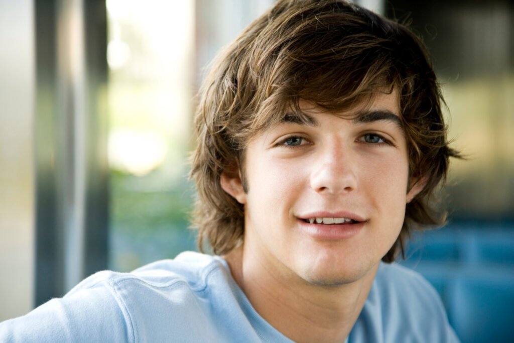 Handsome young man with brown hair and blue eyes smiles gently at the viewer